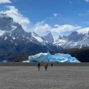Walkers on the grey shore of Lake Grey, with icebergs and the Paine massif behind
