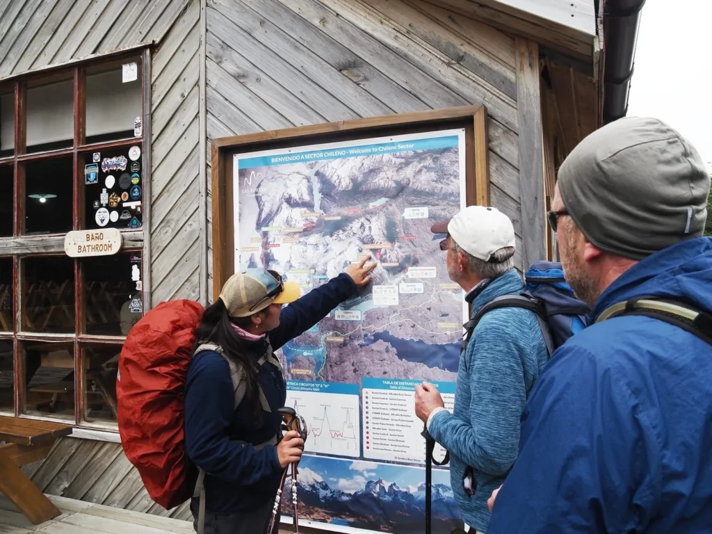 Local guide explaining the W Trek route to two hikers on the trail map at a refugio in Torres del Paine